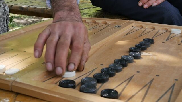 close-up big hands of senior man and young hands of a teenager play backgammon on the board throwing dice and rearranging checkers on the board. board game for gambling people. fortune and luck
