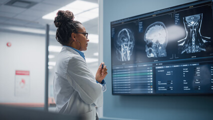 Medical Science Hospital: Confident Black Female Neurologist, Neuroscientist, Neurosurgeon, Looks at TV Screen with MRI Scan with Brain Images, Thinks about Sick Patient Treatment Method. Saving Lives - Powered by Adobe