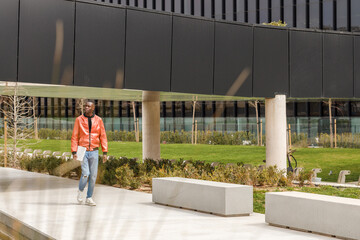 African American guy with laptop walking along park after working day