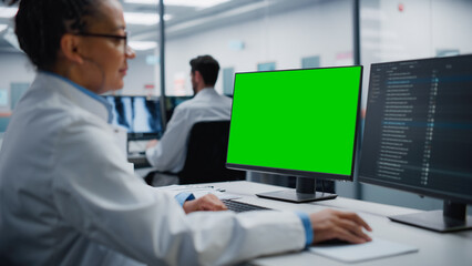 Black Female Medical Doctor is Working on Computer with Green Screen Mock Up Display in a Hospita. African American Scientific Professional Doing Biotehnology Treatment Research in Modern Hospital