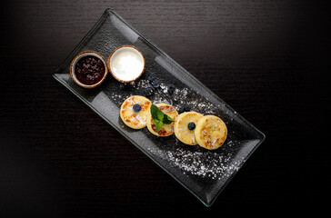 Breakfast, cheesecakes with two sauces. mint and blueberries, on a dark background