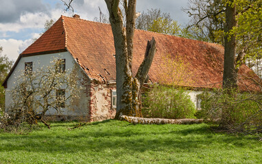 An old stone house. Red tile roof, wooden details. Green garden. Spring, early summer. Idyllic rural scene. Architecture, exterior design, building traditions, countryside living, tourism themes - obrazy, fototapety, plakaty