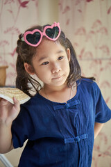 Asian little girl in hat and sunglasses posing while wearing dark blue dye cotton shirt.