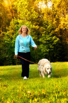 happy smiling blond woman with her dog white golden retriever walking in nature 

