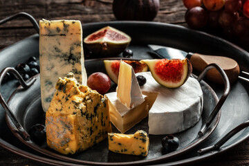 Various kind of cheese, traditional pieces of french, italy and spanish manchego cheese with grapes and figs served on wooden table