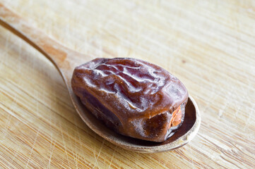 Organic dried hurma dates medjool grains, in wooden spoon on cutting board - obrazy, fototapety, plakaty