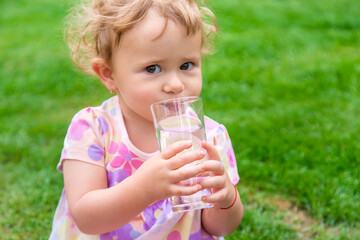 Baby drinks water from a glass. Selective focus.