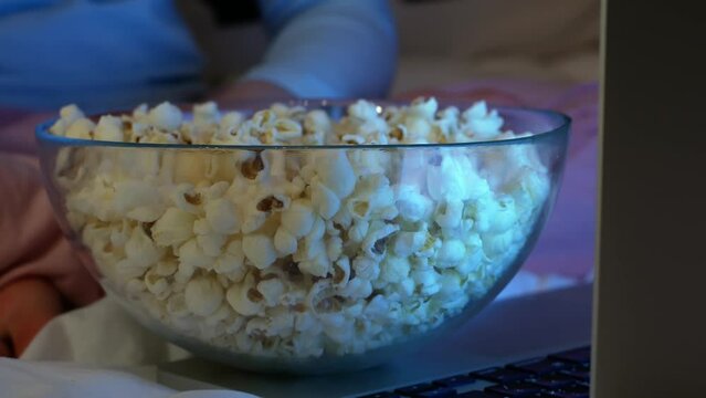 Little kids watch TV at home and eat popcorn.