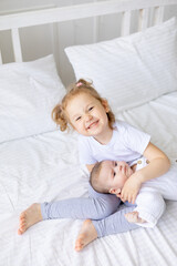 Fototapeta na wymiar a little girl hugs a newborn sister or brother on a white bed at home, two children in the family