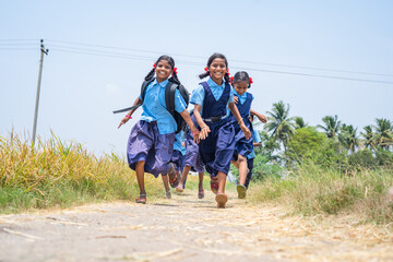group of school girls running home in race after school near farm land at village - concept of...