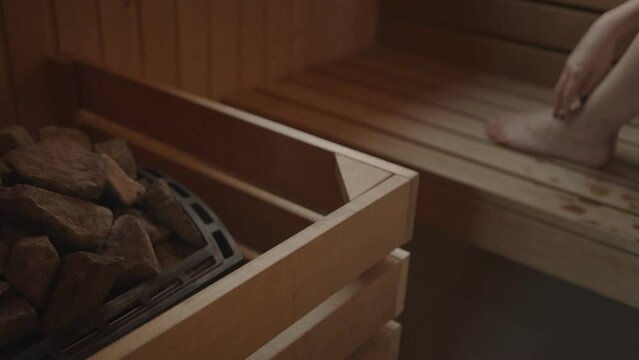 Woman relaxing and sweating in hot sauna. Real, authentic sauna moment. Sauna stove and stone.