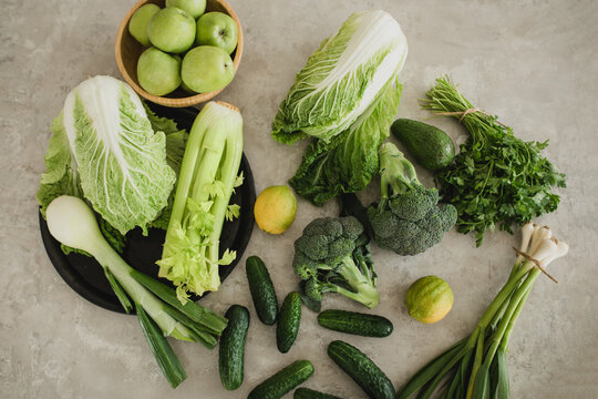 Still life with green fruit and vegetables on grey table.