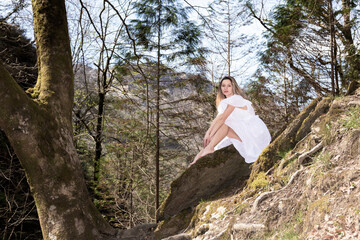 blonde woman in white dress sitting on a rock in the forest