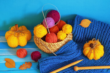 Autumn knitting and hobby concepts. Yellow knitted pumpkins, colorful balls of wool, warm scarf, knitting needles and autumn leaves on blue rustic table