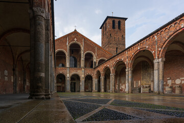 Saint Ambrogio church brick building with bell towers, courtyard, arches at overcast day, Milan,...