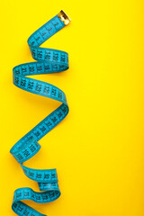 Blue plastic measure tape with metric scale over on color yellow background. Vertical photo.