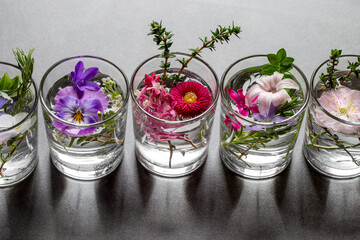 Fünf kleine Glasvasen mit duftenden Frühlingsblumen stehen in einer Reihe auf grauem Untergrund