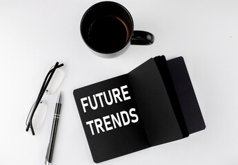 FUTURE TRENDS written text in small black notebook with coffee , pen and glasess on white...