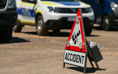 Road traffic sign used during a car crash accident. The word accident is spelled on the sign. Police car in background. Road safety.