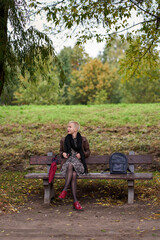Cheerful young short haired blonde woman sitting on the bench and relaxing in the autumn park.
