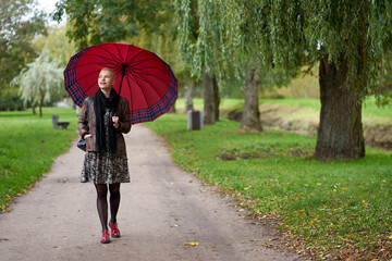 Attractive smilling short haired blonde woman walking in the autumn park with huge red umbrella.