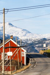 scenic route in Norway close to Utne  with a traditional red houses norwegian and snowy mountain