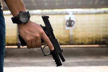 A gun shooter holds 9mm automatic pistol in right hand in front of the gun shooting range, concept for security, robbery, gangster and bodyguard training around the world. selective focus on pistol. - obrazy, fototapety, plakaty