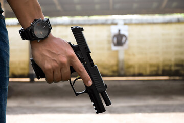 A gun shooter holds 9mm automatic pistol in right hand in front of the gun shooting range, concept...