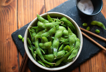 Steamed edamame sprinkled with sea salt on a dark stone board, top view