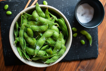 Steamed edamame sprinkled with sea salt on a dark stone board, top view