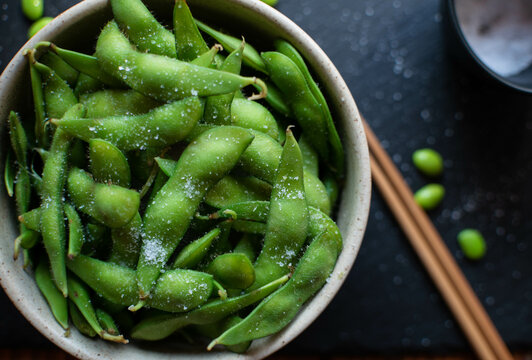 Close-up of steamed edamame sprinkled with sea salt on a dark stone board, top view