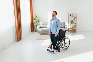 Disabled young guy trying to get up from wheelchair at home, copy space.