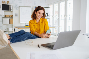 Young woman taking a break in the office and looking at her cell phone