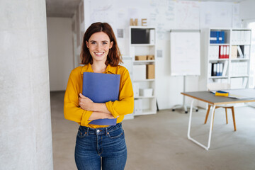 Young student stands in an office with her application documents and laughs into the camera