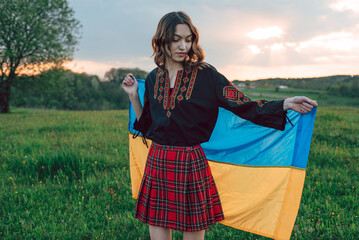 horizontal portrait of young Ukrainian woman in vyshyvanka  - ukrainian national clothes. She is holding ukrainian flag - symbol of freedom and independence. Stand with Ukraine