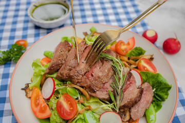 A gourmet dish featuring sliced meat on a bed of fresh greens, garnished with tomatoes and radishes, set on a checkered tablecloth.
