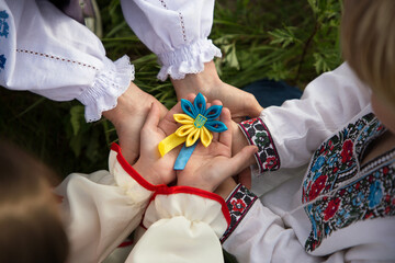 children's and adult hands in embroidered shirts carefully in unity hold blue-yellow symbol trident...