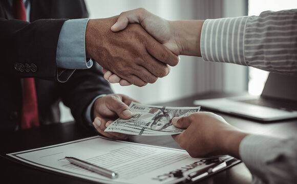 Shaking Hands With Congratulations On An Evil Plan, Businessmen Give Dollars To Bribe Employees In Signing Contracts To Buy Illegal Land And Real Estate, Corruption And Bribery Concept.