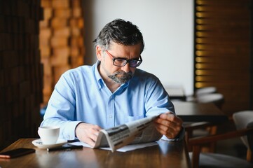 active senior man reading newspaper and drinking coffee in restaurant