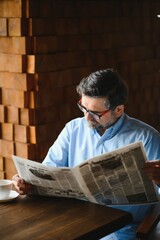active senior man reading newspaper and drinking coffee in restaurant