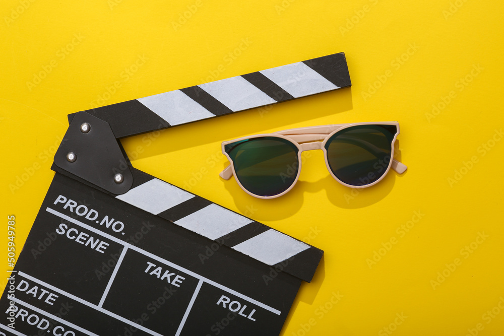 Wall mural movie clapperboard with sunglasses on a yellow bright background. top view