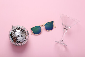 Minimal party concept. Sunglasses with a disco ball and cocktail glass on pink background. Top view