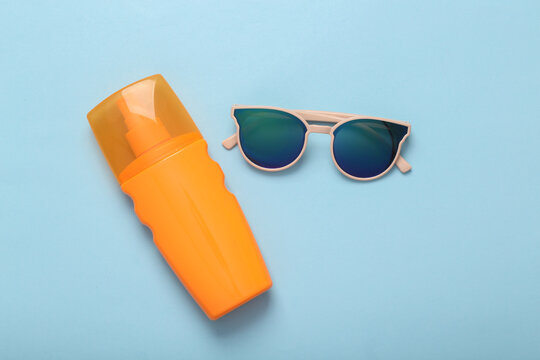 Resort, beach vacation, vacation concept. Sunglasses and a bottle of tanning cream on a blue background. Top view