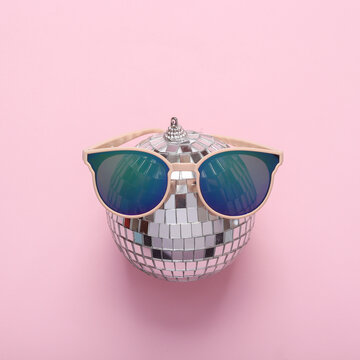 Minimal party concept. Sunglasses with disco ball on pink background. Top view