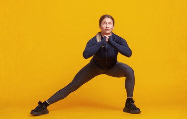 Fototapeta na wymiar Workout concept. Young athletic woman in sportswear practicing side lunges on a yellow studio background. Fitness, aerobics, healthy lifestyle