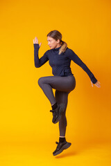 Fototapeta na wymiar Athletic woman in sportswear jumps up on a yellow background. dynamic movement. Aerobics, healthy lifestyle, fitness concept