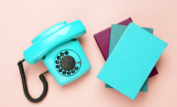 Retro old fashioned blue rotary phone and books on pink background. Top view