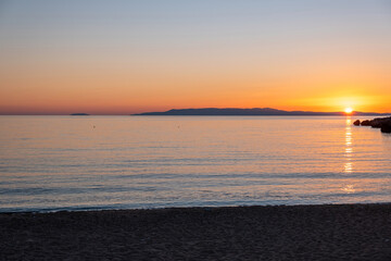Sandy beach at sunset. Greece. Sundown over calm sea, reflection and orange color sky.