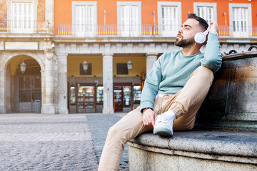young man sitting on the street listening to music with wireless headphones. High quality photo