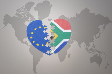 puzzle heart with the national flag of european union and south africa on a world map background. Concept.